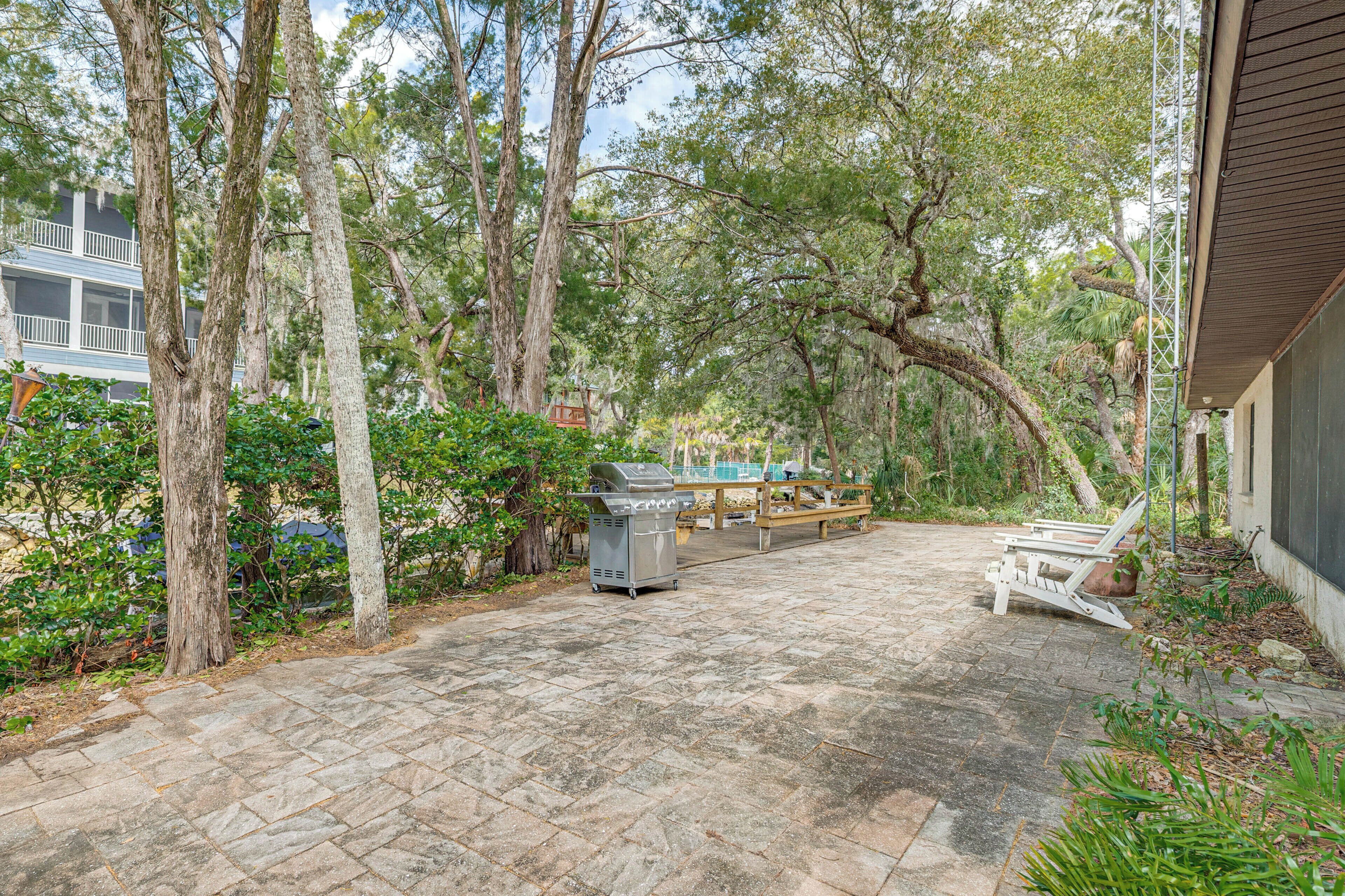 A patio with a grill, wooden deck, and surrounding trees.
