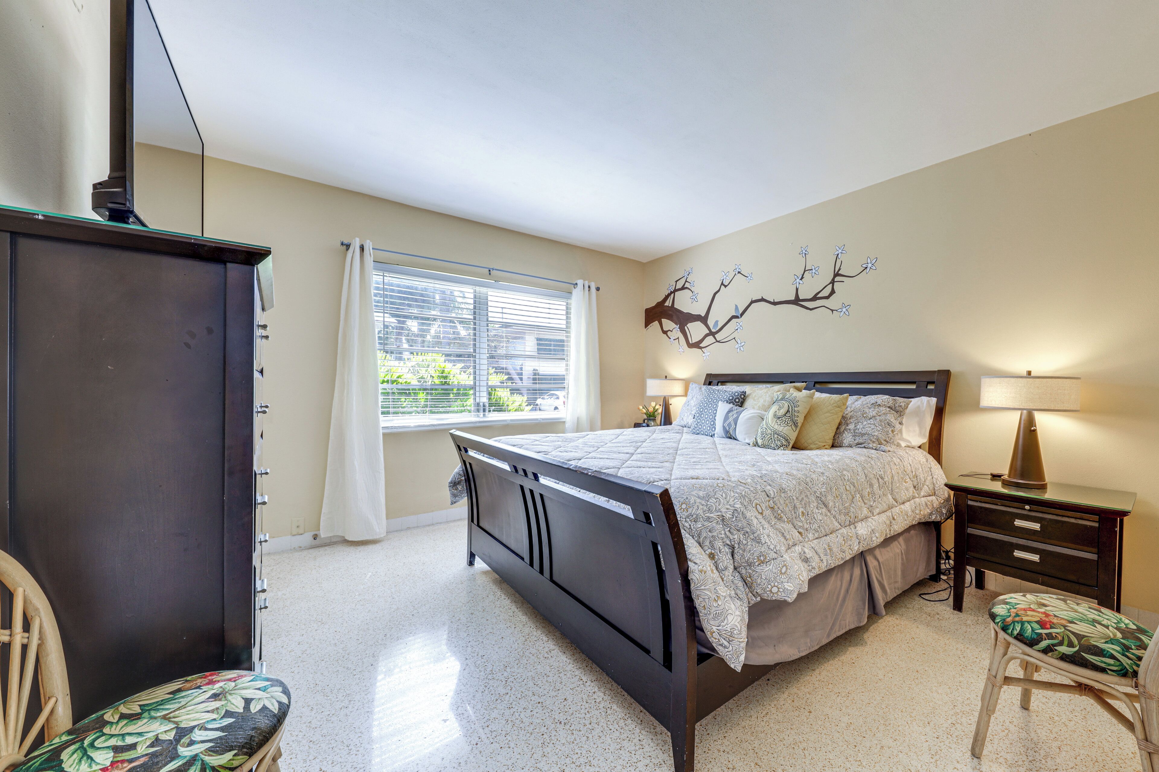 Une chambre à coucher comprenant un lit, des tables de chevet, une commode, une chaise et une fenêtre avec des rideaux.
