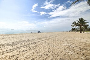 Una extensa playa de arena con palmeras y cielo despejado.