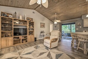 A spacious living room with a large TV, wooden shelves, wicker furniture, and a ceiling fan. - 1 Mi to Boat Launch: Crystal River Home w/ Dock (Crystal River)