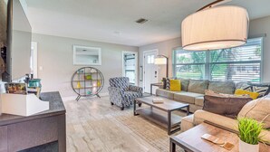 A modern living room with a sofa, armchair, coffee table, and a large window with blinds. - Dock, Kayaks & Bicycles: Crystal River Getaway! (Crystal River)