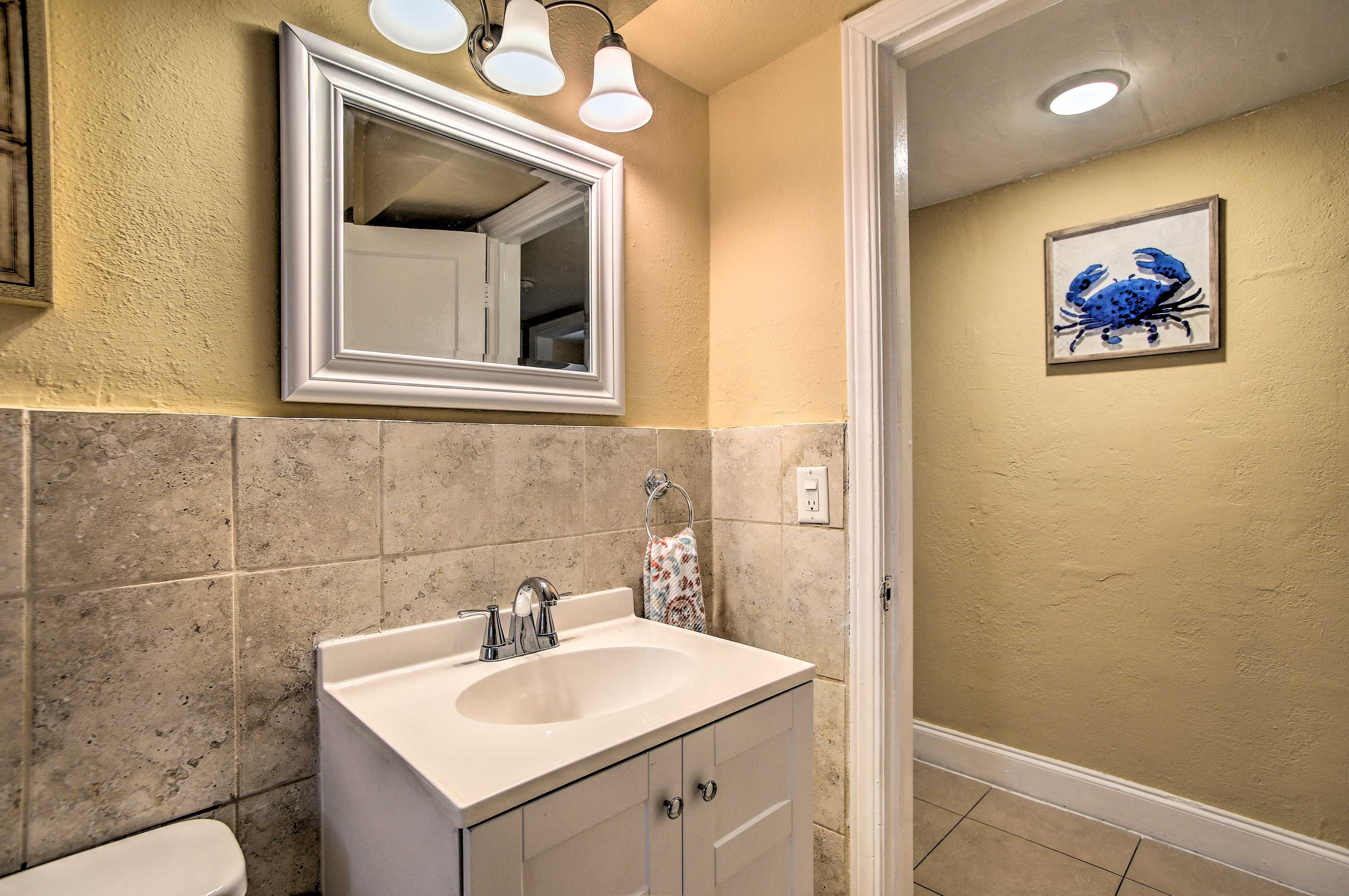 A bathroom with a white sink, a mirror, and a framed artwork on the wall.