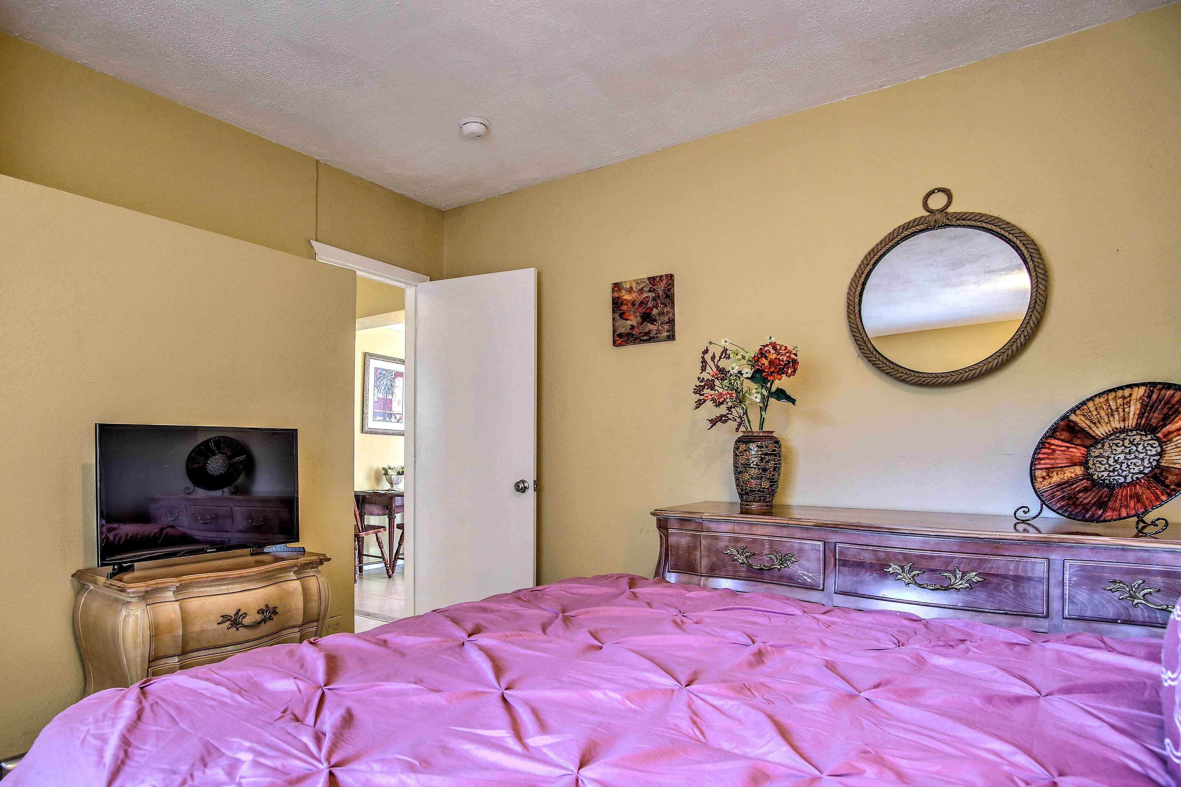 A bedroom with a bed, dresser, TV, and artwork.