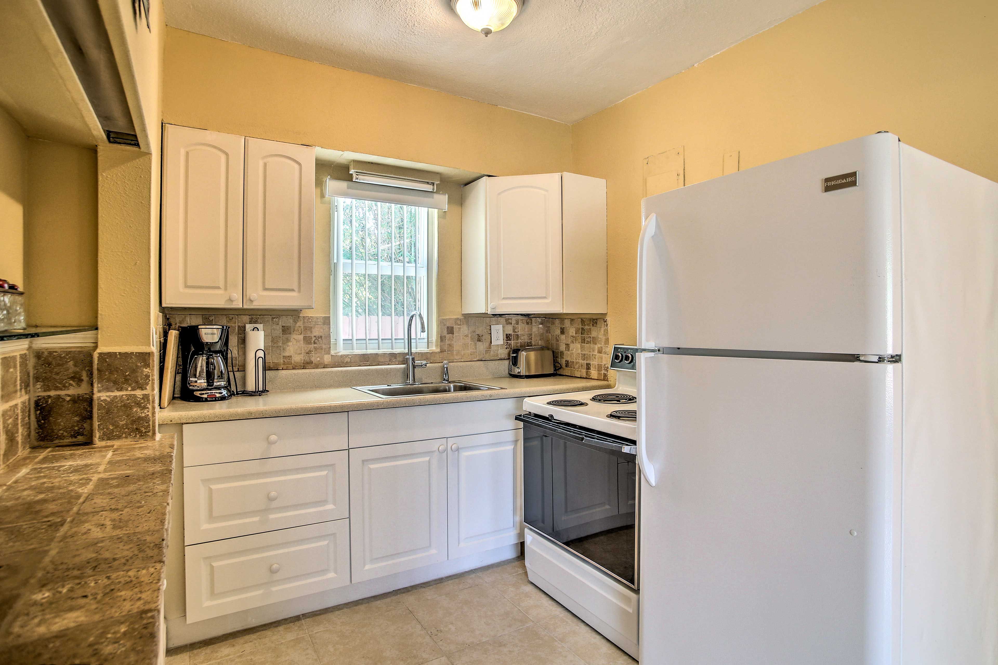 A compact kitchen with white cabinets, a built-in oven, a refrigerator, and a window above the sink.
