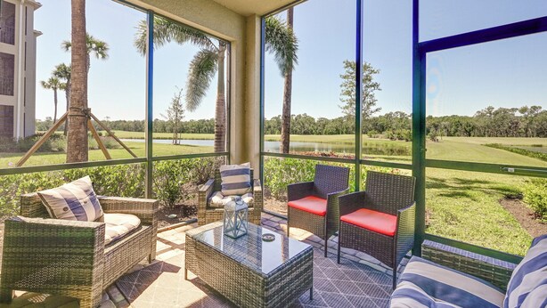 A sunlit patio with wicker furniture and a glass table, overlooking a golf course and palm trees. - Lakewood National Condo w/ Pool Access! (Bradenton)