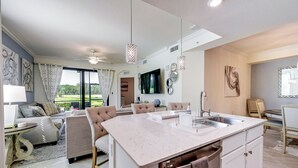 A modern kitchen with a large island, a dining area with a table and chairs, and a living room with a sofa and a TV. - Lakewood National Condo w/ Pool Access! (Bradenton)
