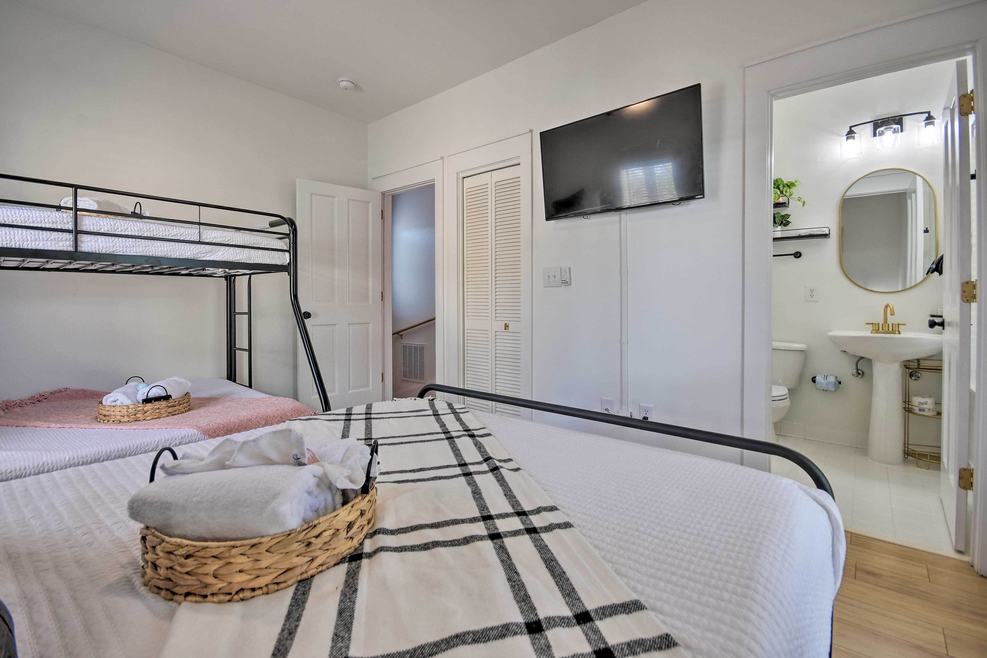 Un dormitorio con literas, un televisor de pantalla plana, un baño con lavamanos y espejo, y una puerta que da a otra habitación.