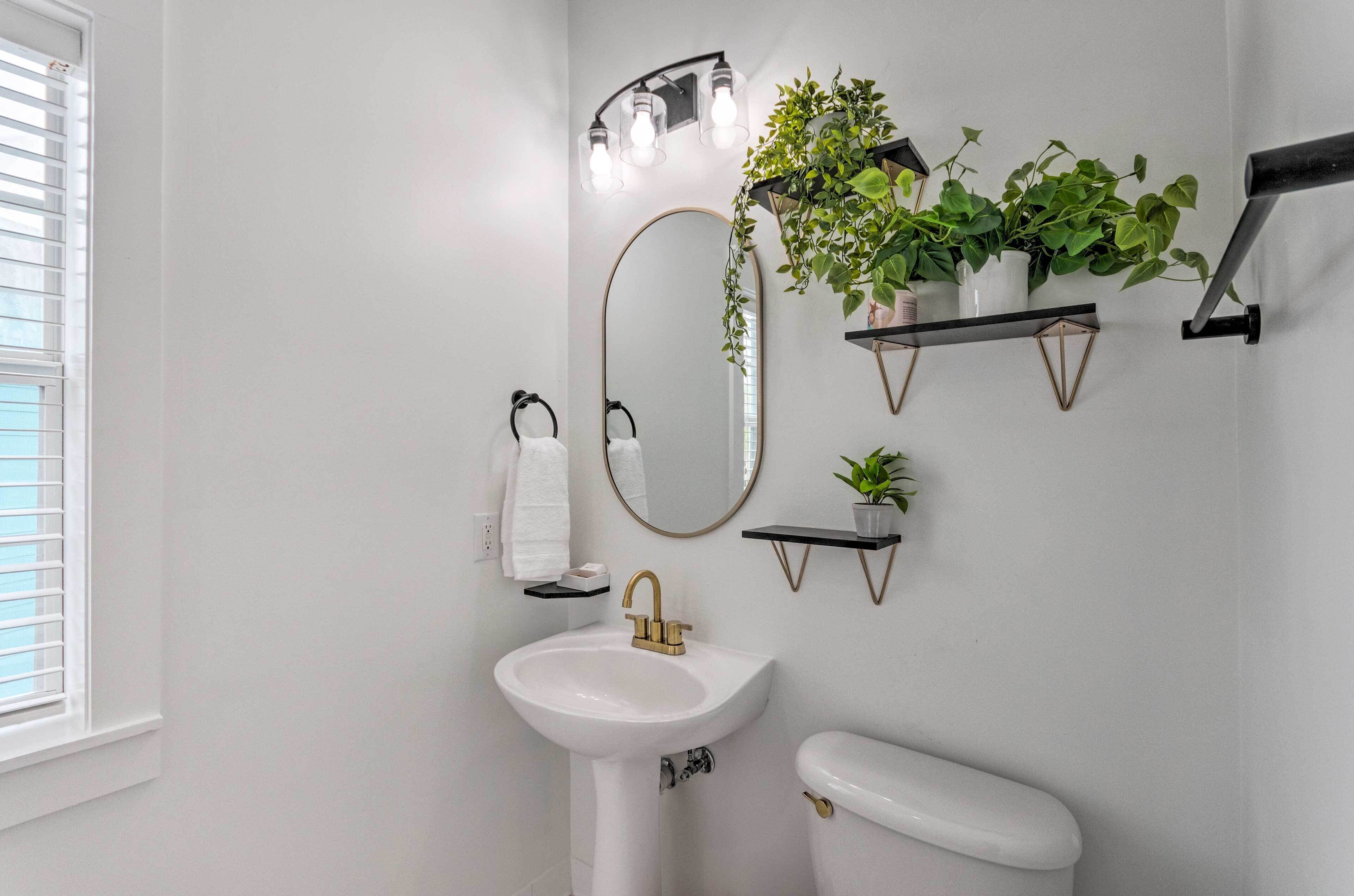 Une salle de bain avec un lavabo blanc, des toilettes, un miroir et des étagères murales ornées de plantes.