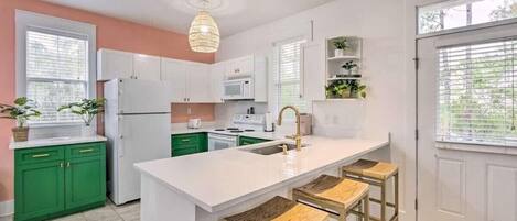 Una cocina moderna con armarios blancos, una isla central, encimeras verdes y blancas y taburetes de bar.