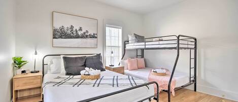 A bedroom with a bunk bed, a bedside table with a lamp, a framed picture on the wall, and a window with blinds.