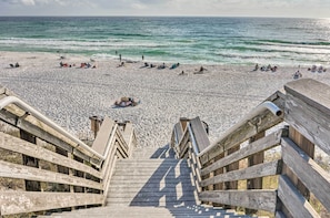 Un escalier en bois descend vers une plage où des gens se prélassent au soleil et se baignent.