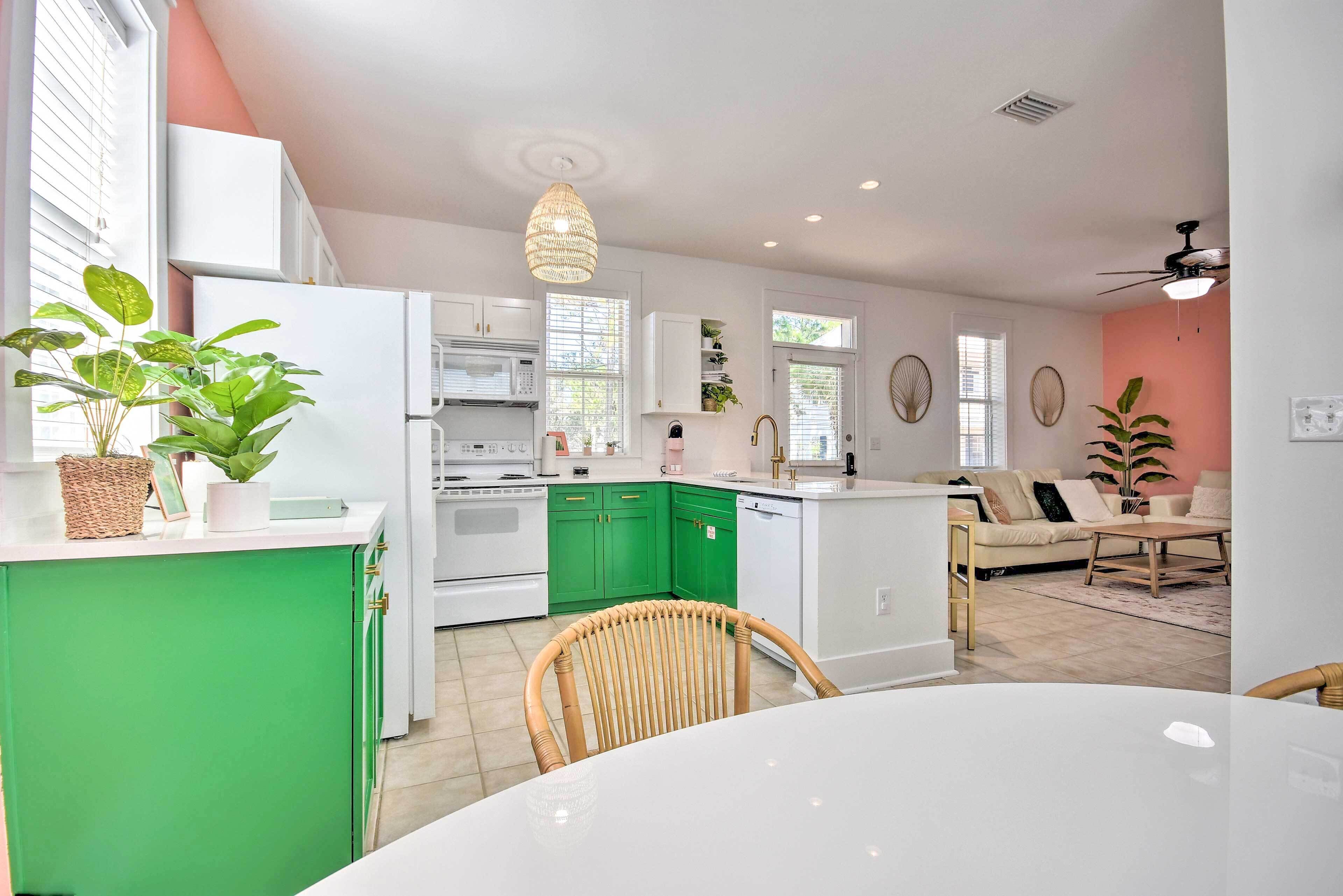 A modern kitchen with green cabinets, white appliances, and a dining area with a white table and wicker chairs.