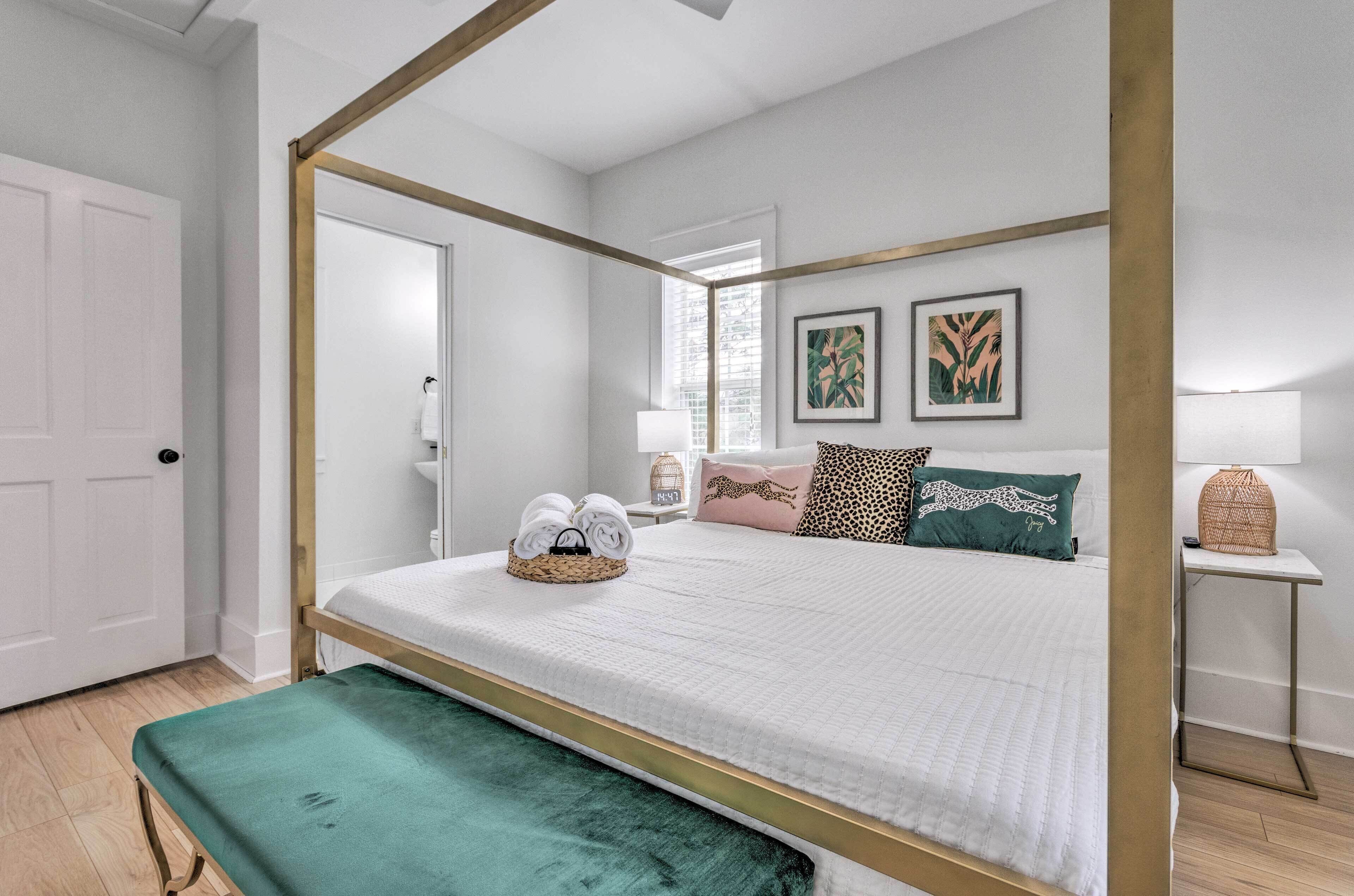 A four-poster bed with a white and gold frame, a teal bench, and two framed artworks on the wall.