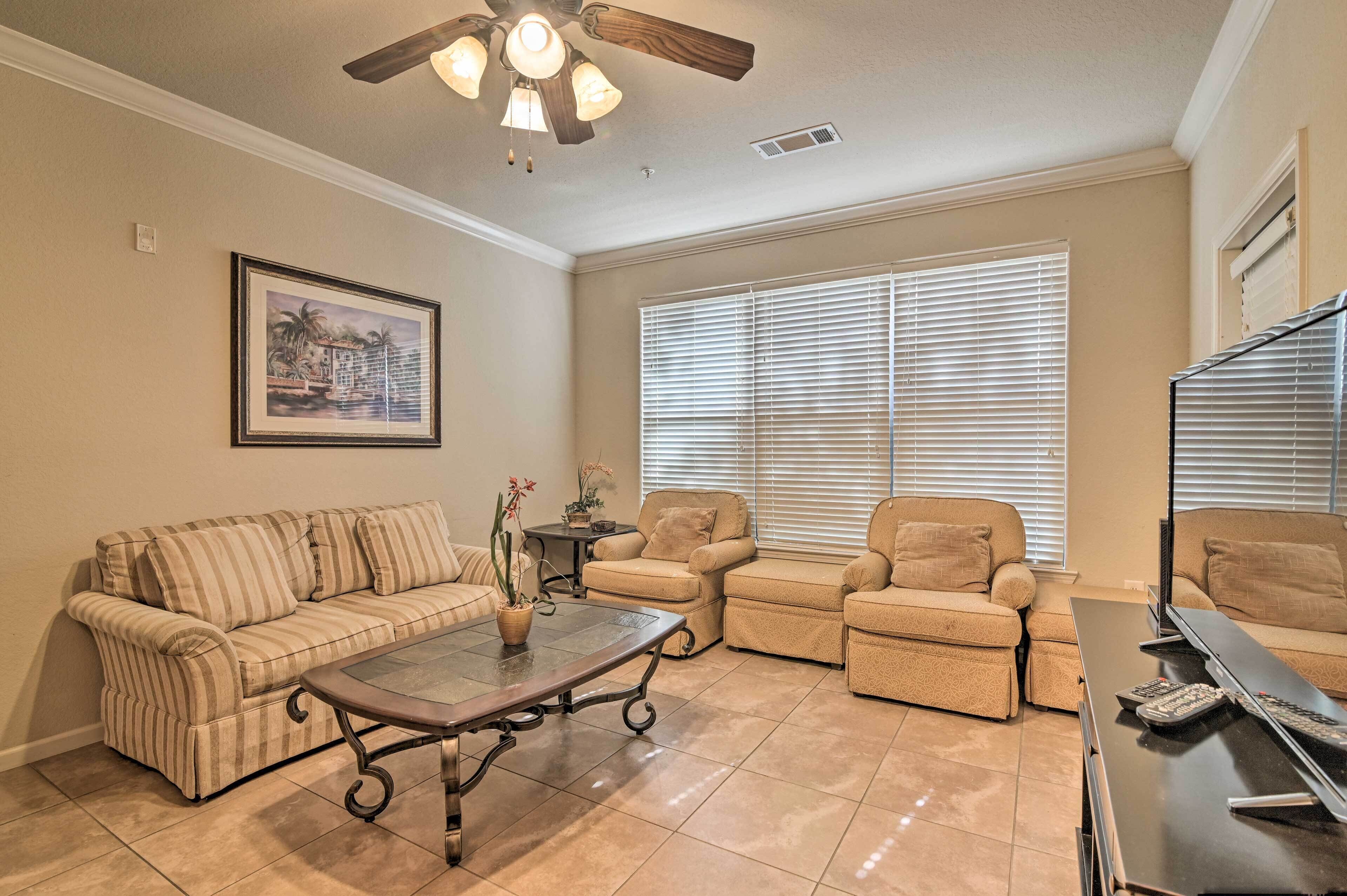 A living room with a beige sofa, two armchairs, a coffee table, and a television.