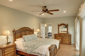 A bedroom with a wooden bed, nightstands, a dresser, a ceiling fan, and a mirror.