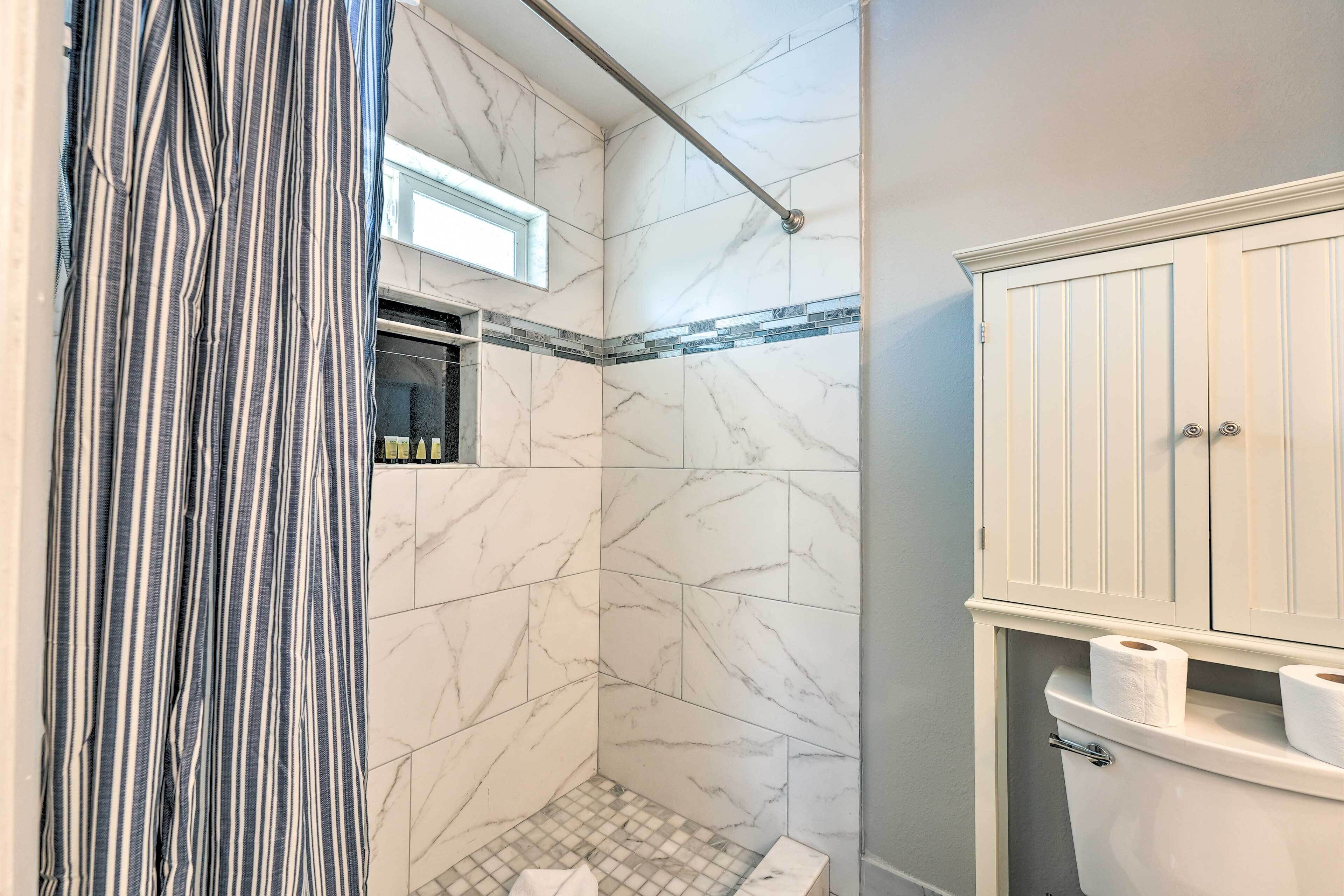 A bathroom with a shower, marble walls, a striped curtain, and a toilet with paper.