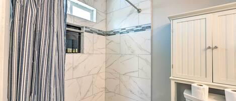 A bathroom with a shower, marble walls, a striped curtain, and a toilet with paper.
