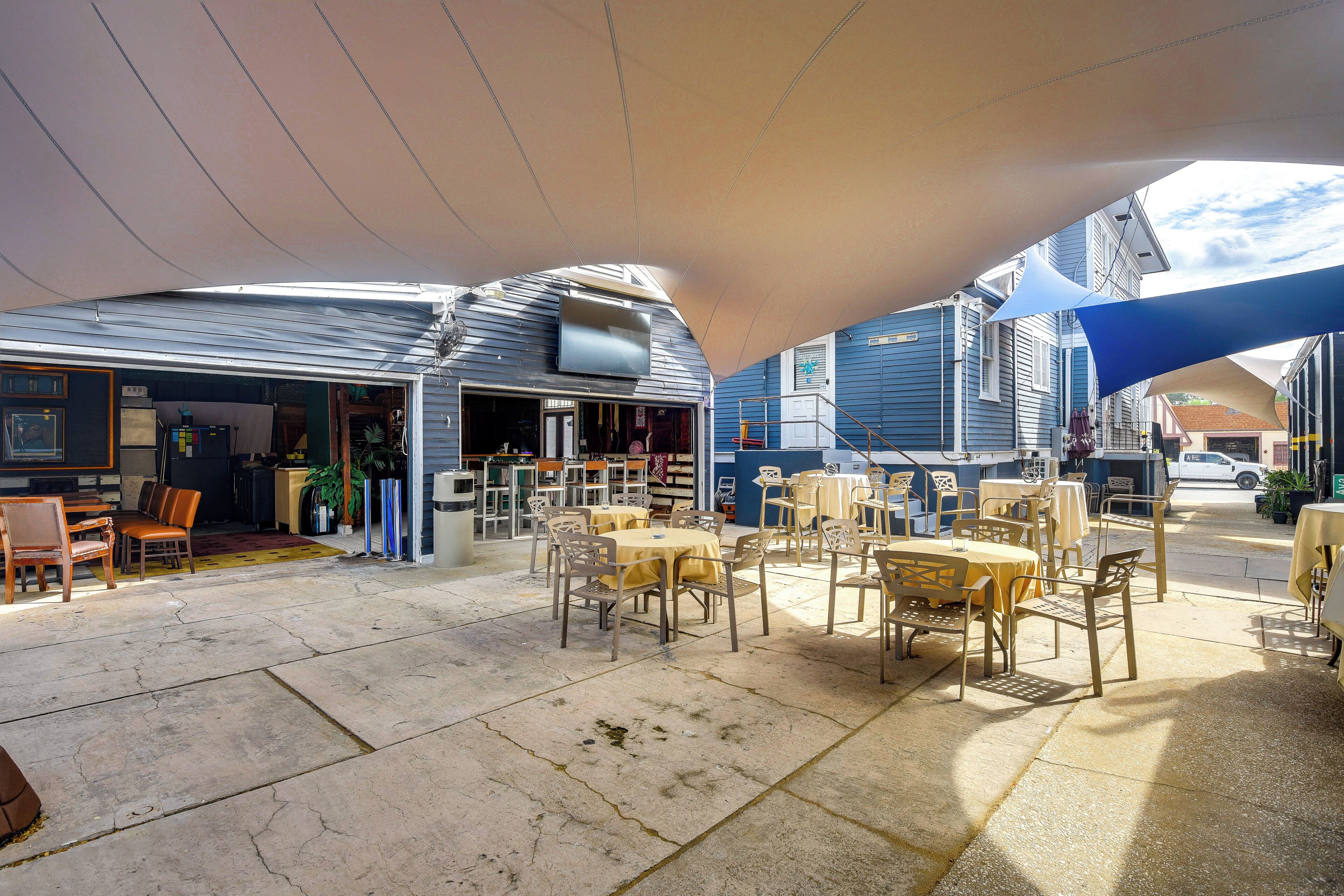 An outdoor seating area with tables and chairs, a covered section with a TV, and a building with a blue exterior.