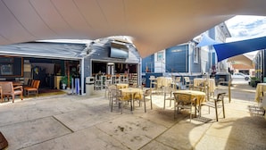 An outdoor seating area with tables and chairs, a covered section with a TV, and a building with a garage door. - Historic Home < 2 Mi to Daytona Beach & Pier! (Daytona Beach)