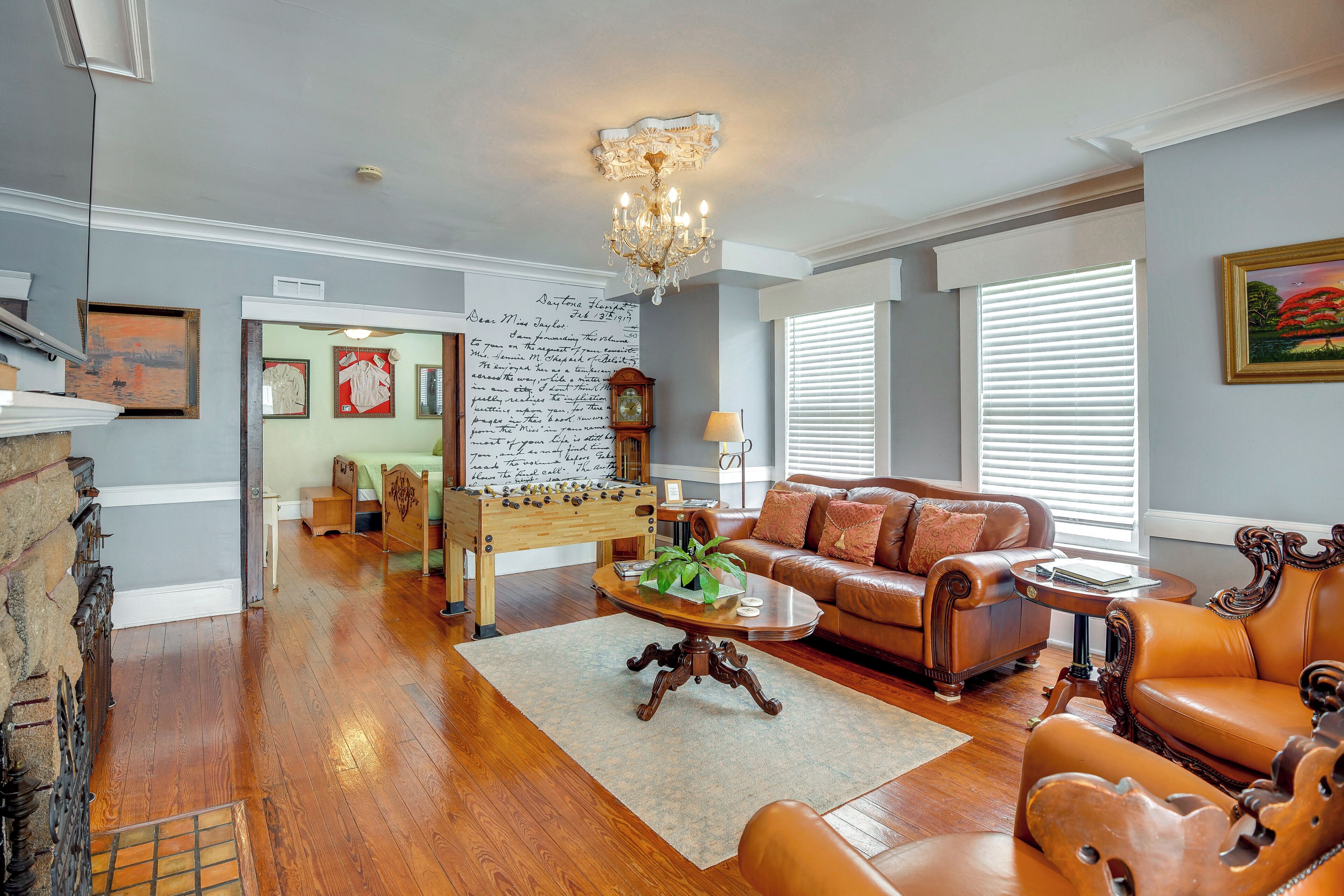 A spacious living room with a brown leather sofa, a wooden coffee table, and a chandelier.