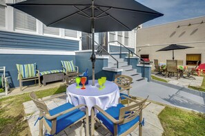 Een terras buiten met een tafel en stoelen, een grote parasol en een barbecue op de achtergrond.