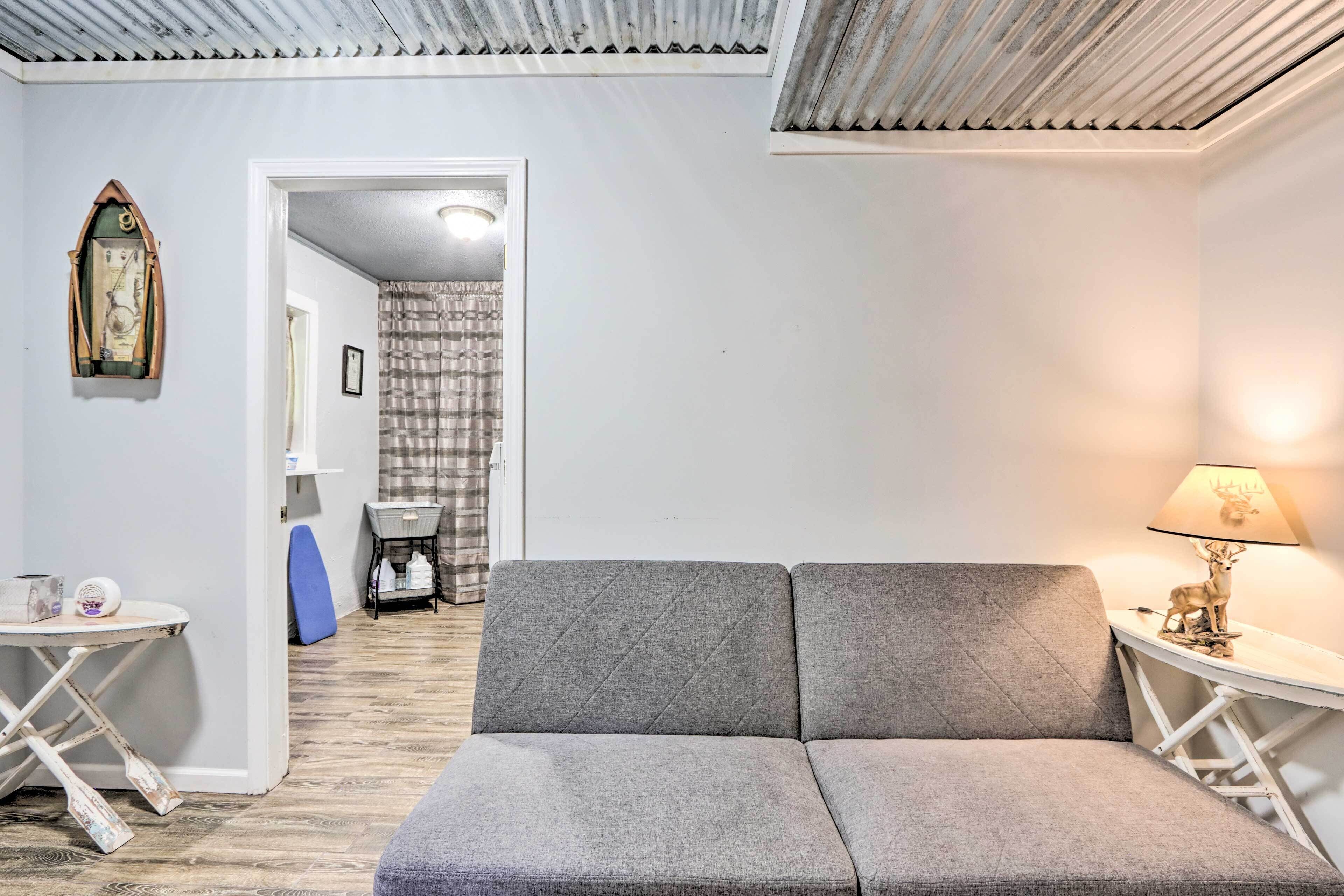 Una habitación acogedora con un sofá gris, una mesita con una lámpara y un reloj en la pared.