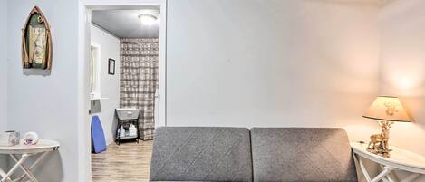 Una habitación acogedora con un sofá gris, una mesita con una lámpara y un reloj en la pared.
