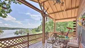 A wooden deck with a glass table and chairs, overlooking a lake.
