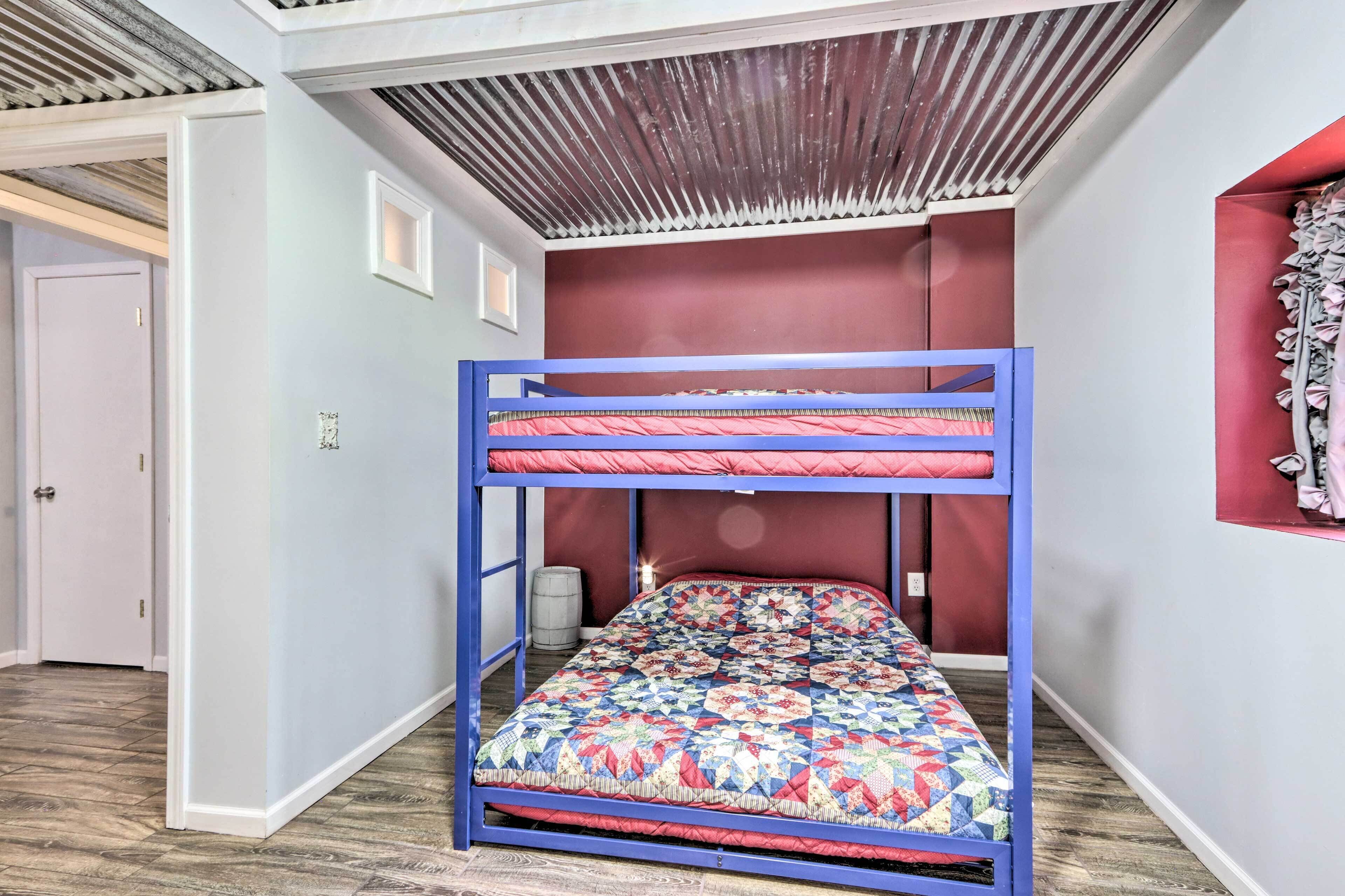 A bunk bed with a colorful quilt, a wooden ceiling, and a red accent wall.
