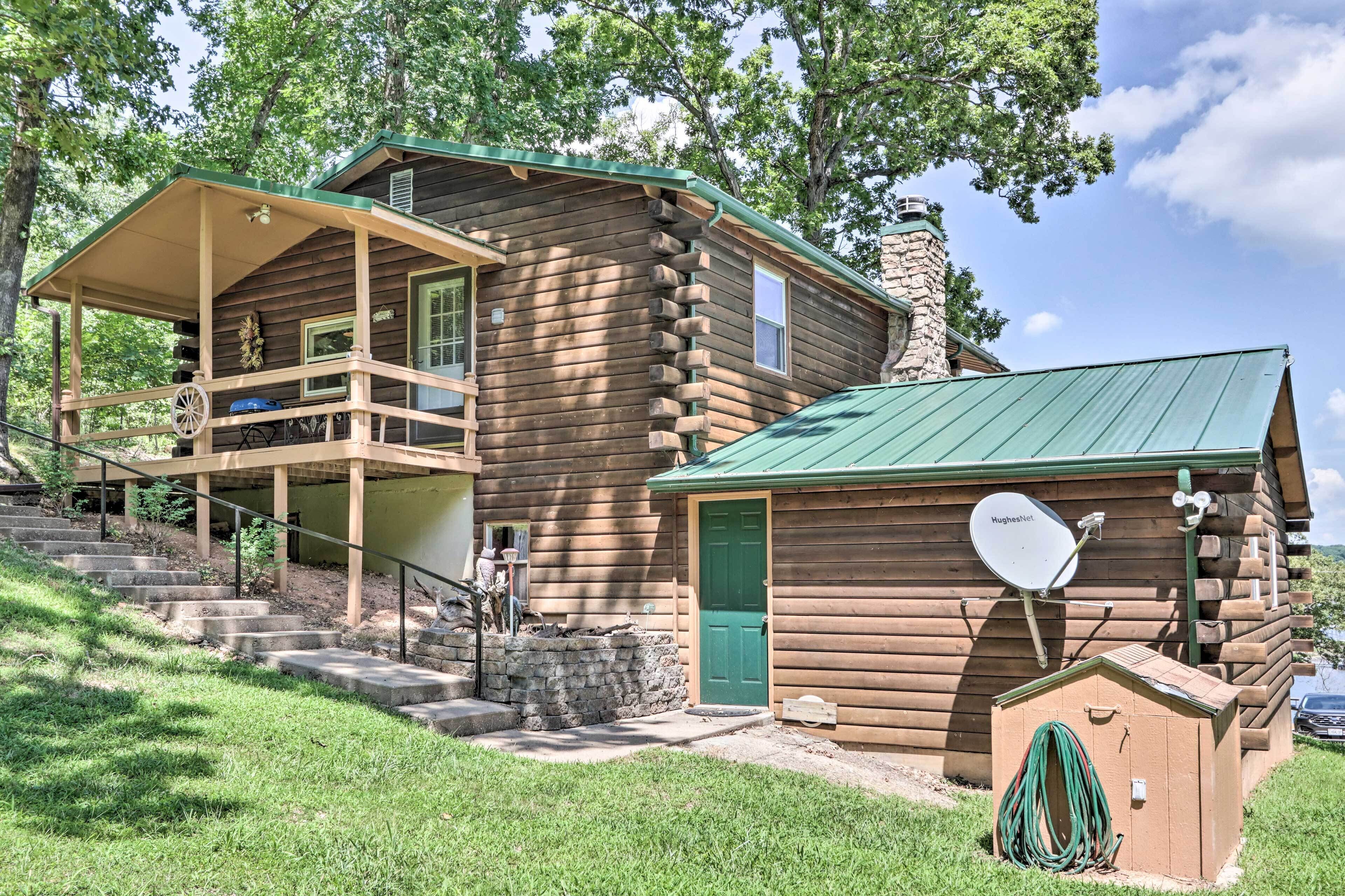A log cabin with a porch, a stone chimney, and a satellite dish.