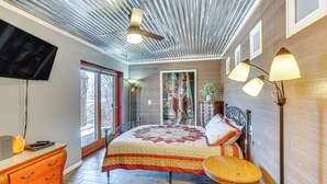 A bedroom with a bed, a television, a wooden floor, a ceiling fan, and a window.
