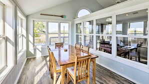 A spacious dining area with a large wooden table and chairs, large windows, and a view of the outdoors. - Cozy Waterfront 'island House' on Live Oak Island! (Crawfordville)