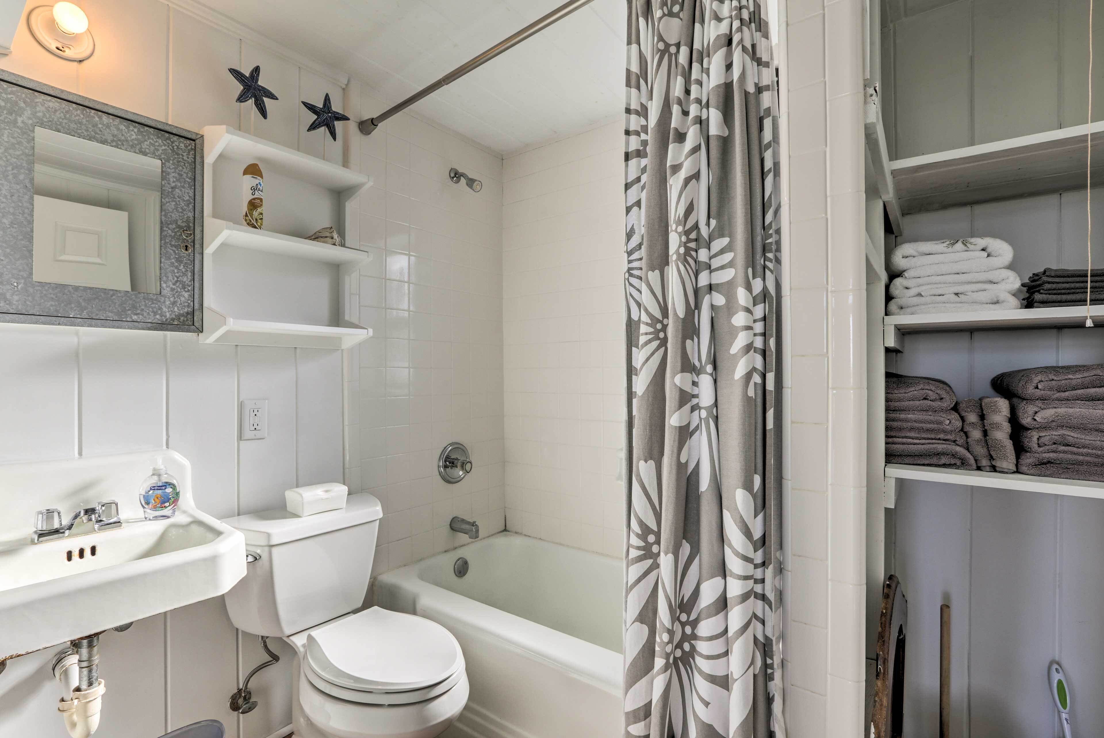 A bathroom with a toilet, sink, and bathtub. Shelves with towels are visible.