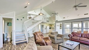 A spacious living room with a high ceiling, a staircase with a white railing, and a leather sofa. - Cozy Waterfront 'island House' on Live Oak Island! (Crawfordville)