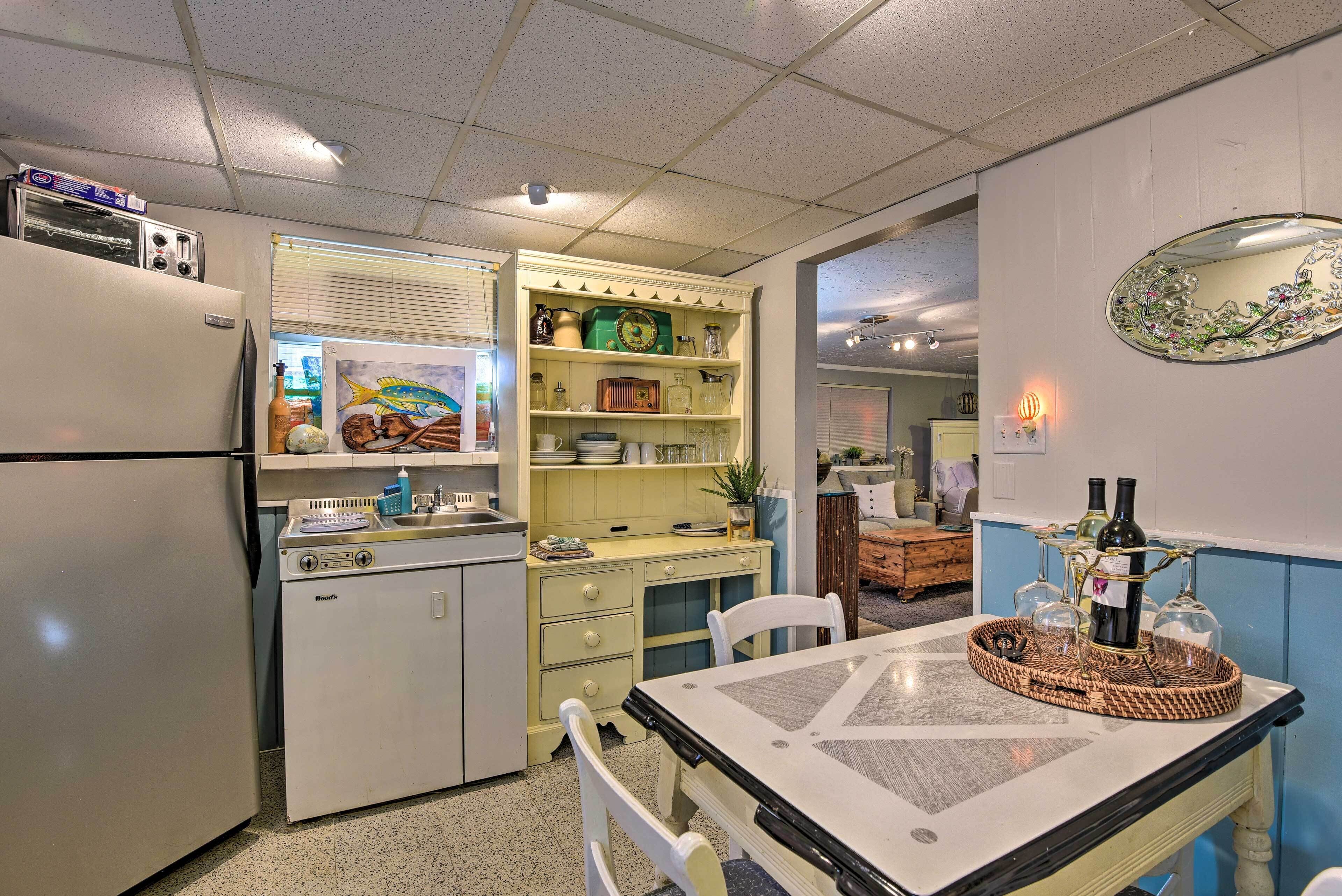 A compact kitchen with a refrigerator, a microwave, and a sink. There is a dining table with chairs and a decorative tray with bottles.