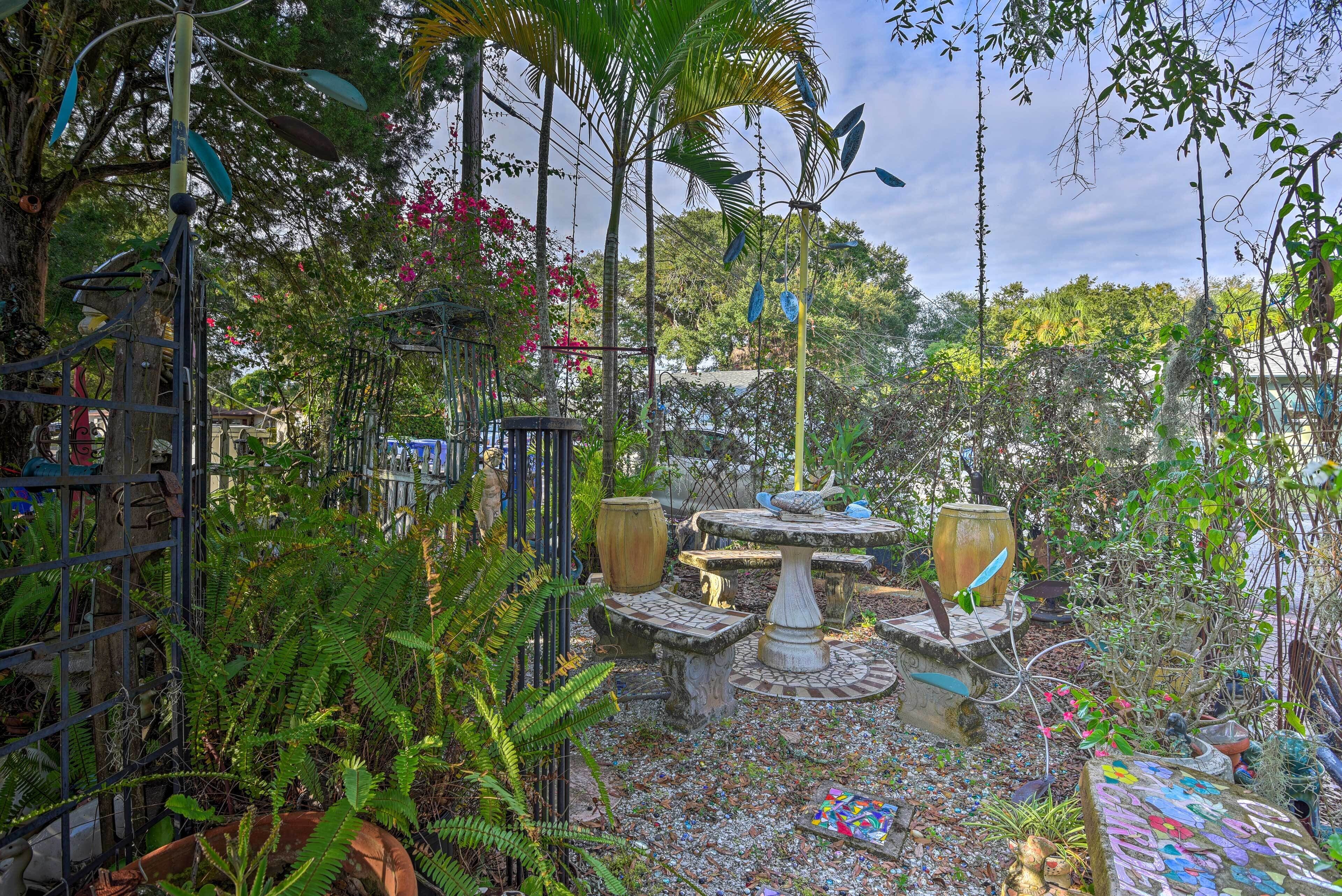 Ein Garten mit einem Brunnen, umgeben von dichtem Grün und einem Metallzaun.