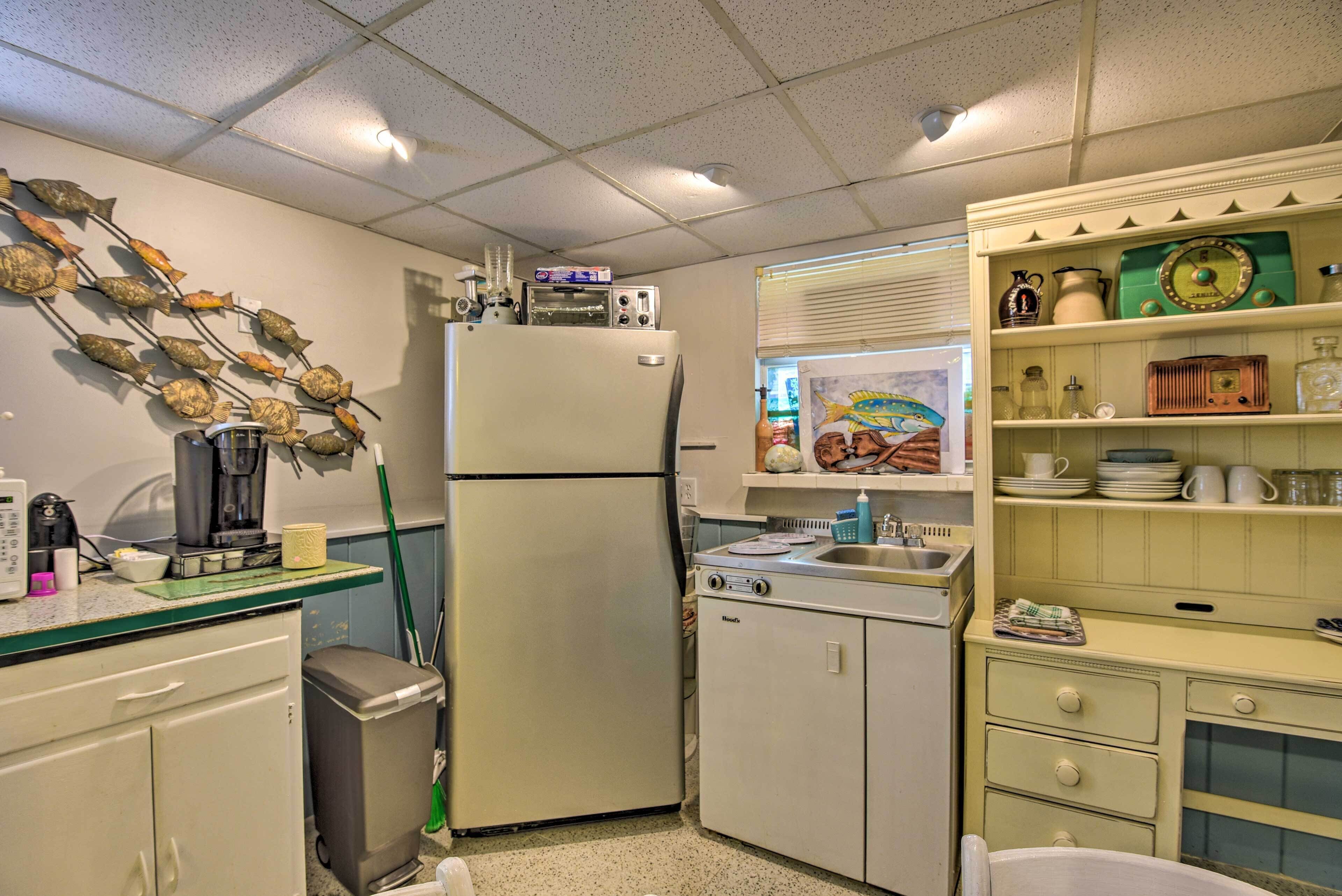 A compact kitchen with a refrigerator, coffee maker, and a microwave. There is a sink and a window with blinds.