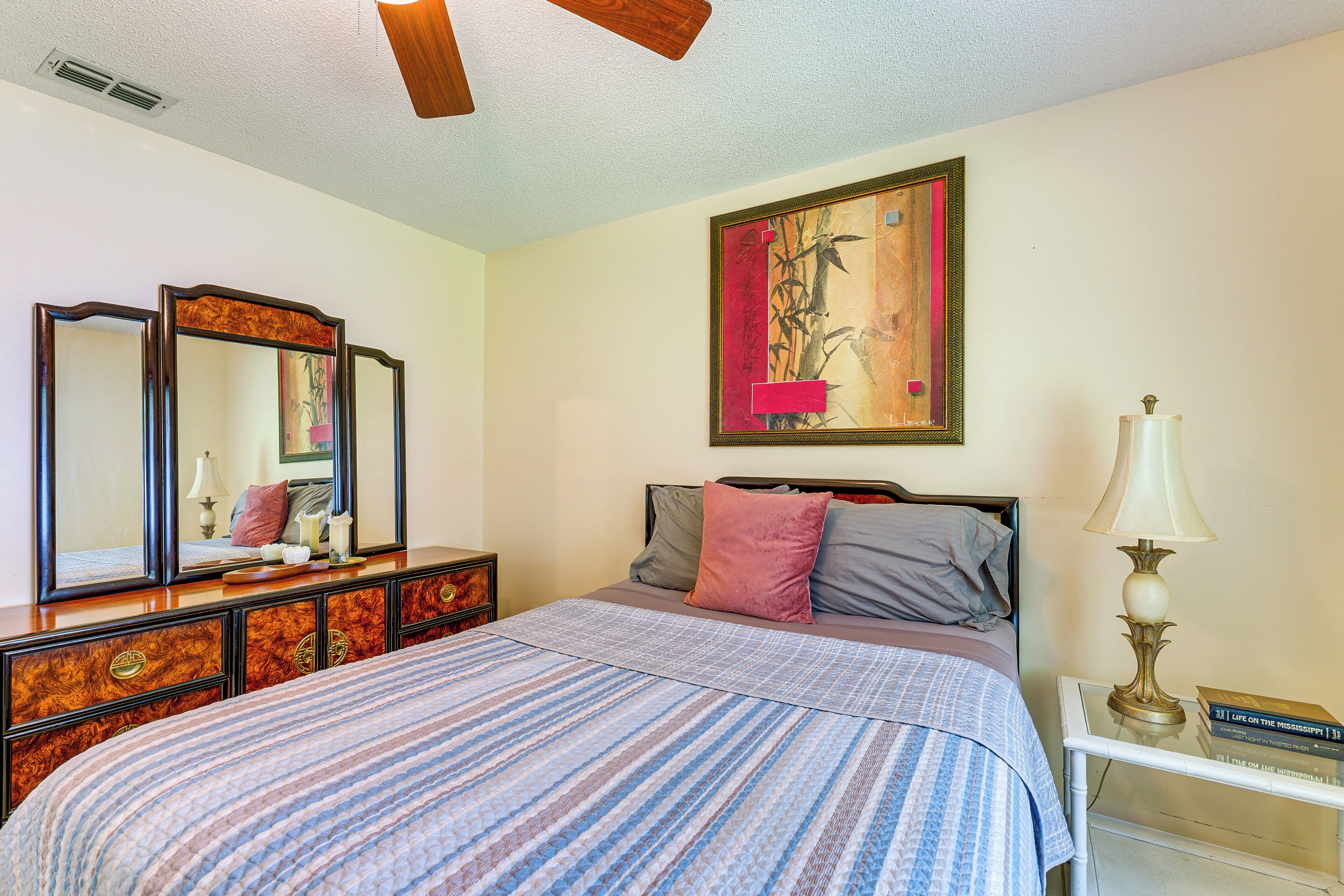 A bedroom with a bed, dresser, bedside table, lamp, and a painting on the wall.