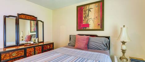 A bedroom with a bed, dresser, bedside table, lamp, and a painting on the wall.