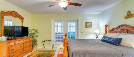 A bedroom with a bed, dresser, television, ceiling fan, windows, and a view of the outdoors.