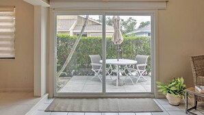 A room with a sliding glass door leading to a patio with a round table and chairs, a potted plant, and a wicker chair. - 'sand Dollar' Jenson Beach Home w/ Pool Access! (Jensen Beach)