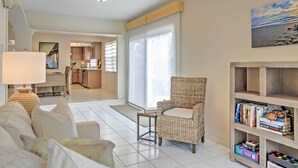 A living room with a sofa, a wicker chair, a small table, and a bookshelf with books and a teddy bear. - 'sand Dollar' Jenson Beach Home w/ Pool Access! (Jensen Beach)