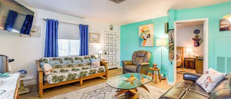 A living room with a sofa, a glass coffee table, a leather couch, and a blue curtain.