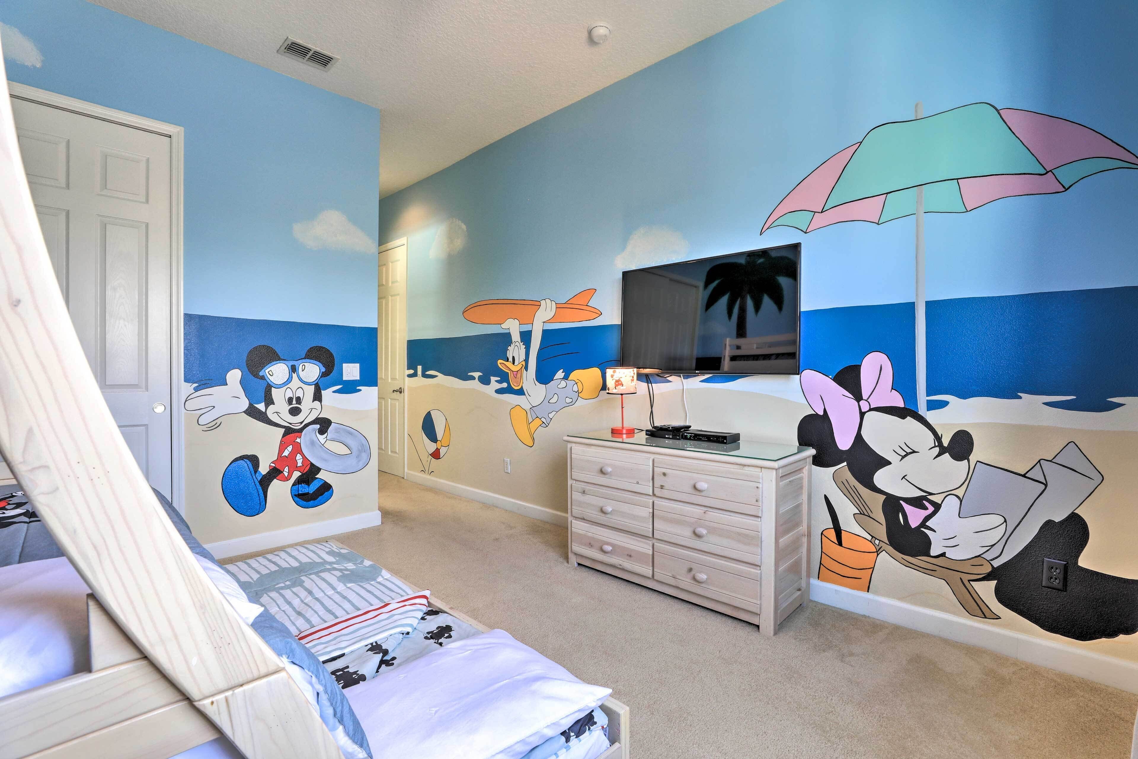 A child's bedroom with Mickey Mouse and Minnie Mouse murals, a bed, a dresser, and a TV on the wall.