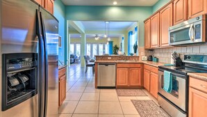 A modern kitchen with stainless steel appliances, wooden cabinets, and a view into the living area.
