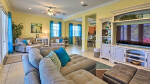 A spacious living room with a large gray sectional sofa, a flat-screen TV, and a ceiling fan.