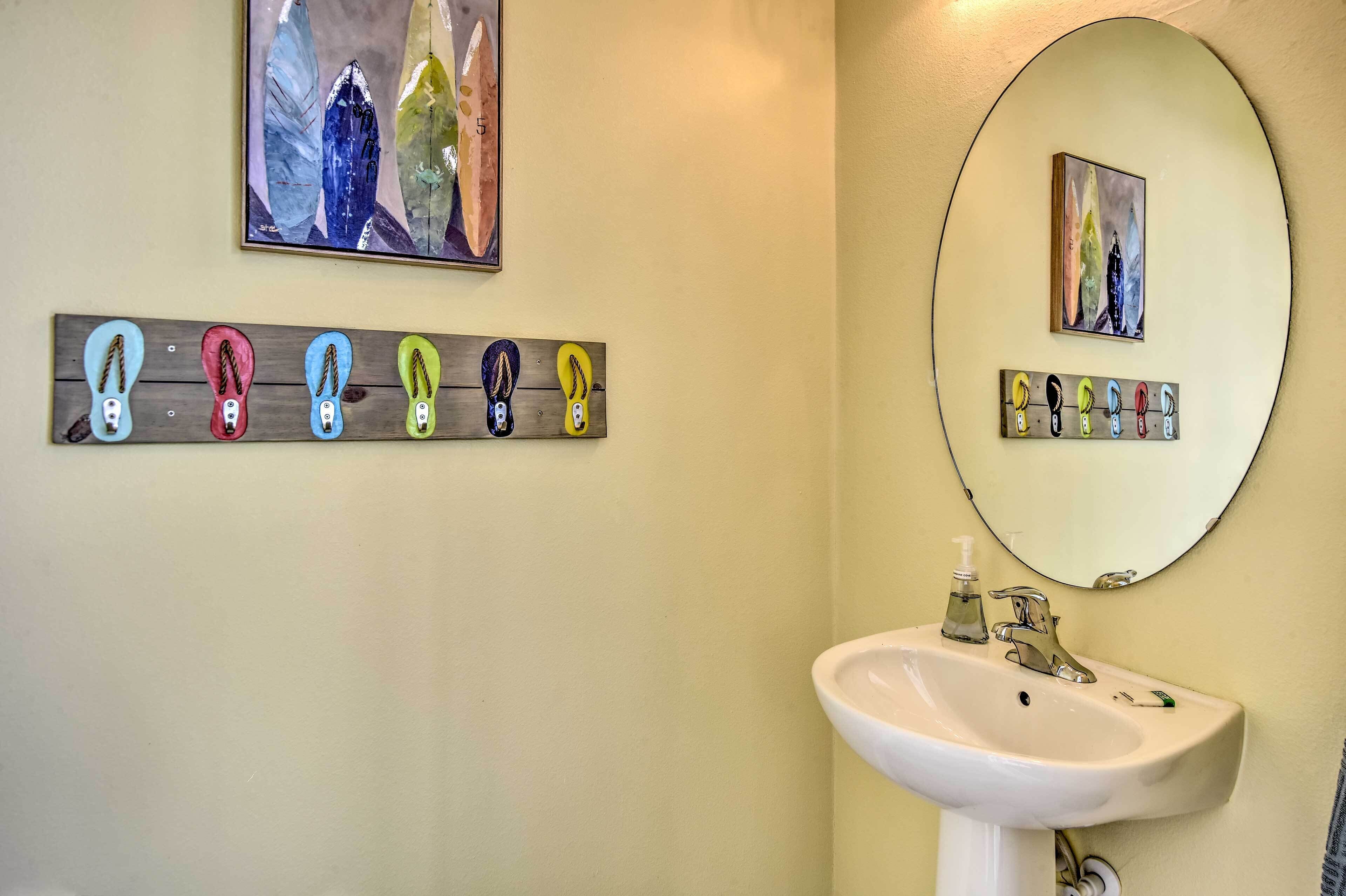 A bathroom with a white sink, a mirror, and a wall-mounted rack holding colorful slippers.