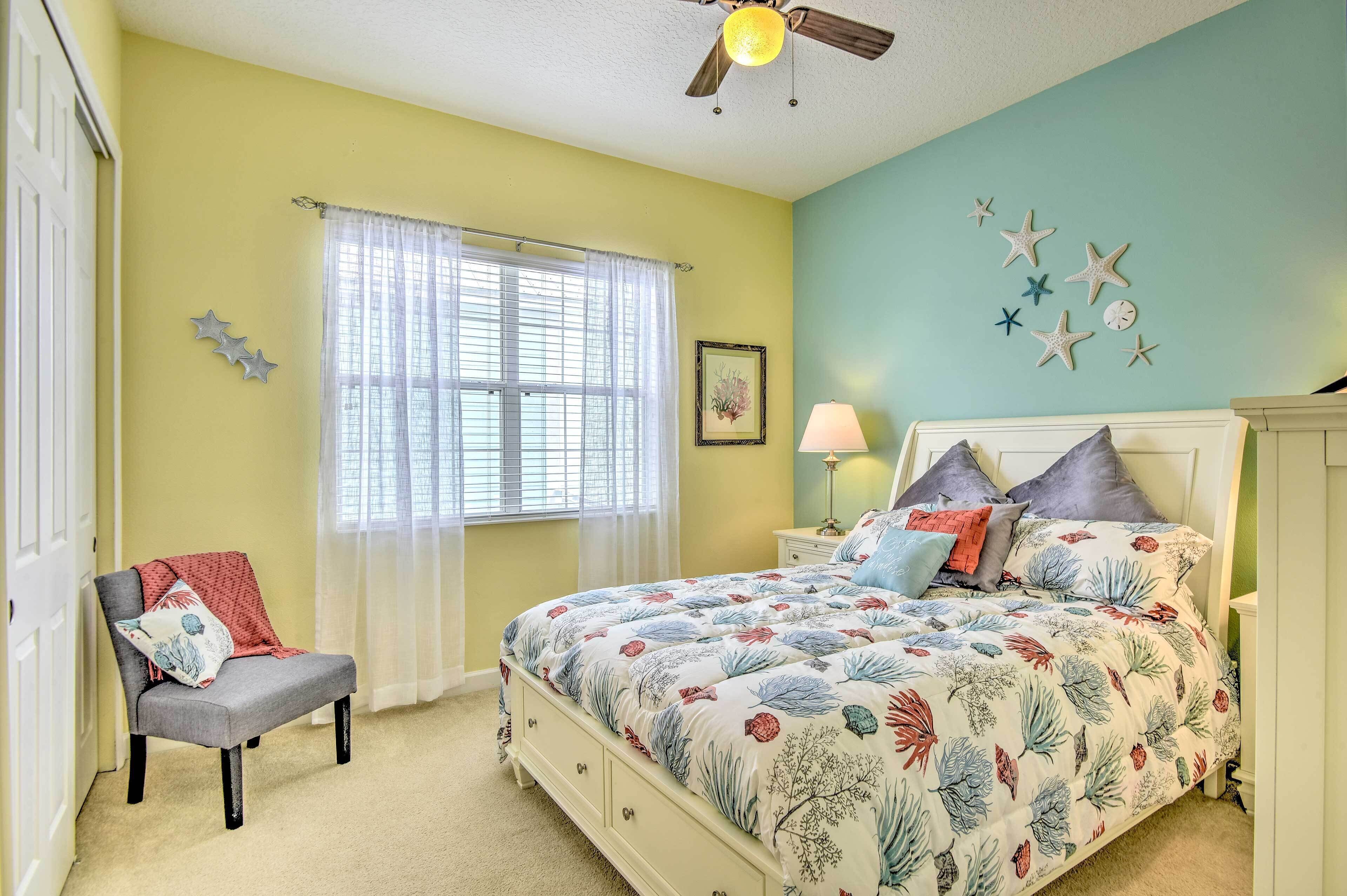 Une chambre à coucher comprenant un lit, une chaise, une fenêtre avec des rideaux, un ventilateur de plafond et des éléments de décoration murale.
