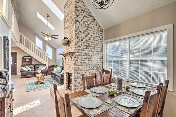 A spacious living area with a high ceiling, a fireplace, and a dining table set for four.