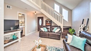 A spacious living room with a large flat-screen TV, leather sofas, a staircase, and a door with a decorative glass window. - A-frame Retreat in Pensacola, 10 Mi to Dtwn (Pensacola)